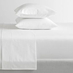 two white pillows on top of a bed with sheets and pillowcases in the background