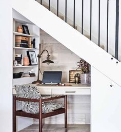 a desk with a laptop on it under a stair case in a home office area