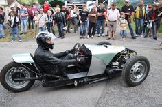 a man riding on the back of a green and white motorcycle with people standing around