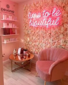 a pink chair sitting next to a table in a room with flowers on the wall