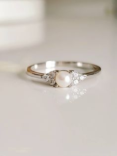 a white pearl and diamond ring sitting on top of a marble countertop next to a mirror