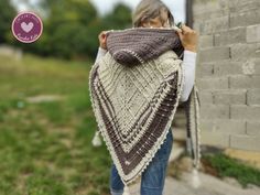 a woman is holding up a shawl in front of a brick wall and grass