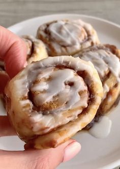 a person is holding some cinnamon rolls on a plate