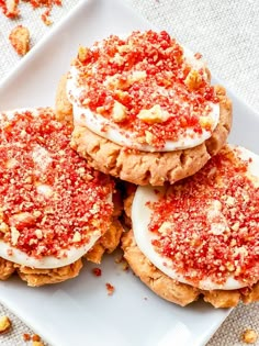 four cookies with white frosting and red sprinkles on a square plate