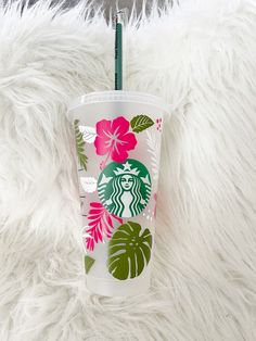 the starbucks cup is decorated with tropical leaves and pink flowers on white furnishing