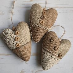 three burlap hearts with buttons are hanging from twine on a white wooden surface