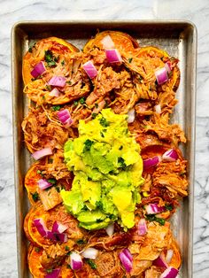 an overhead view of some food in a pan on a marble counter top, with onions and avocado garnishes