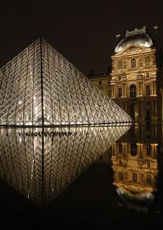 the pyramid is lit up at night in front of a building with its reflection on the water