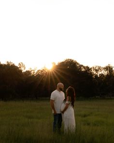 a man and woman standing in a field at sunset