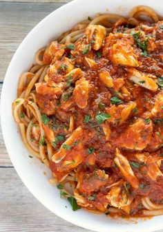 a white bowl filled with pasta covered in sauce and garnished with parsley