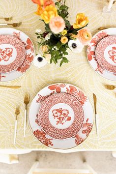 the table is set with red and white plates, silverware, and yellow flowers