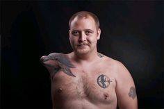 a man with tattoos on his chest standing in front of a black background