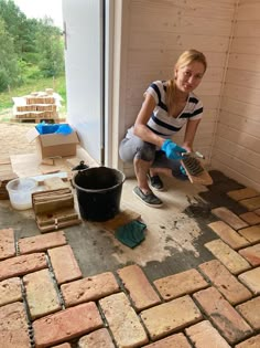 a woman kneeling down on the ground with a brush and bucket in front of her