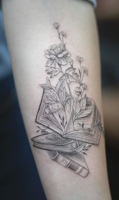 an open book and flowers tattoo on the arm