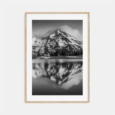 a black and white photo of a snow covered mountain in the distance with water reflecting it's surface