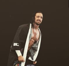 a man with long hair and no shirt standing in front of a black background holding a wrestling belt