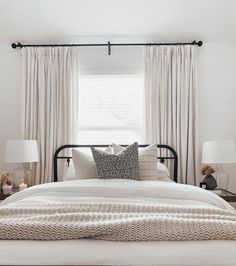 a bed with white sheets and pillows in front of two lamps on either side of the bed