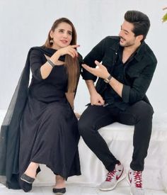 a man sitting next to a woman on top of a white bed in front of a tree