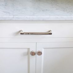 a white kitchen with marble counter tops and cupboard pulls on the doors, which are also stainless steel handles