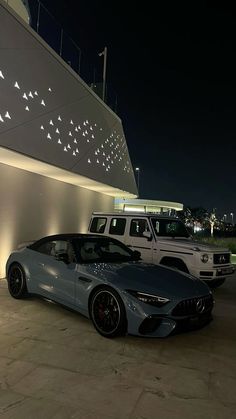 two cars parked next to each other in front of a building at night with lights on