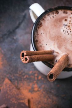 two cinnamon sticks sticking out of the top of a cup of hot chocolate with cocoa powder