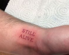 a person with a small tattoo on their arm that says still alive in red ink