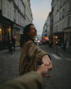 a man holding the hand of another person on a city street at dusk with buildings in the background