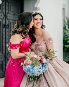 two women in dresses hugging each other with flowers on the bouquet and one woman wearing a pink dress