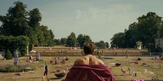 a woman sitting on top of a bench covered in a pink towel next to trees