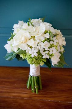 a bouquet of white flowers sitting on top of a wooden table next to a blue wall