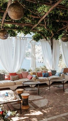 an outdoor seating area with white drapes and lots of pillows on the couches