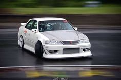 a white car driving down a race track with trees in the backgrouund