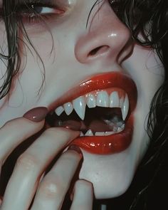 a close up of a person with red lipstick and fangs on her face, holding their hand to the mouth