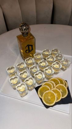 a table topped with lots of glasses filled with liquid and lemon slices next to a bottle