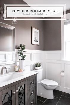 a white toilet sitting next to a sink in a bathroom under a window with framed pictures on the wall