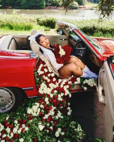 a woman sitting in the back of a red convertible car with flowers on it's floor