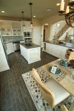 a dining room table and chairs in a kitchen with white cabinets, wood floors and an open staircase leading up to the second floor