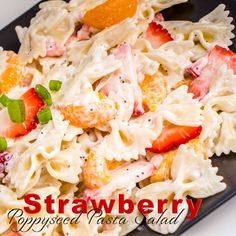 a black plate topped with pasta covered in cheese and strawberries next to an orange