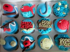 cupcakes decorated with blue frosting and various types of fishing related items are displayed in a box