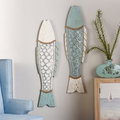 two wooden fish hanging on the wall next to a blue chair and potted plant