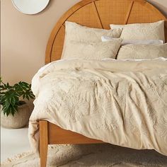 a bed with white linens and pillows in a neutral colored room next to a potted plant