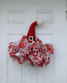 a red and white christmas wreath hanging on the front door with santa's hat