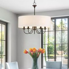 a vase with flowers sitting on top of a dining room table next to two windows