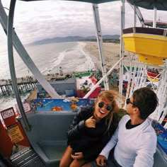 a man and woman sitting on top of a ride at an amusement park next to the ocean