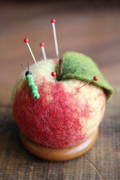 an apple with some pins in it and a green leaf on the top, sitting on a wooden surface