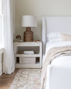 a white bed sitting next to a lamp on top of a wooden table in a bedroom