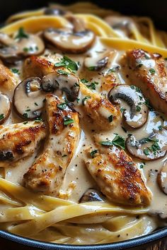 pasta with chicken, mushrooms and sauce in a black bowl on a wooden table top