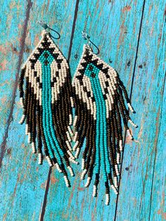 two pairs of beaded earrings with black, white and blue feathers on wooden planks