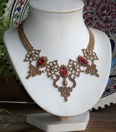 a necklace is displayed on a white mannequin next to a potted plant