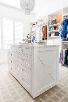 an organized closet with white drawers and gold hardware on the bottom drawer, along with a chandelier hanging from the ceiling